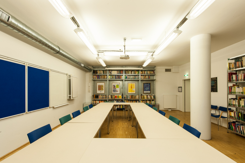 leerer Seminarraum im C3. In der Mitte des Raumes steht ein langer Tisch mit Stühlen. An der Wand hängt ein Whiteboard