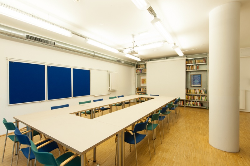 leerer Seminarraum im C3. In der Mitte des Raumes steht ein langer Tisch mit Stühlen. An der Wand hängt ein Whiteboard