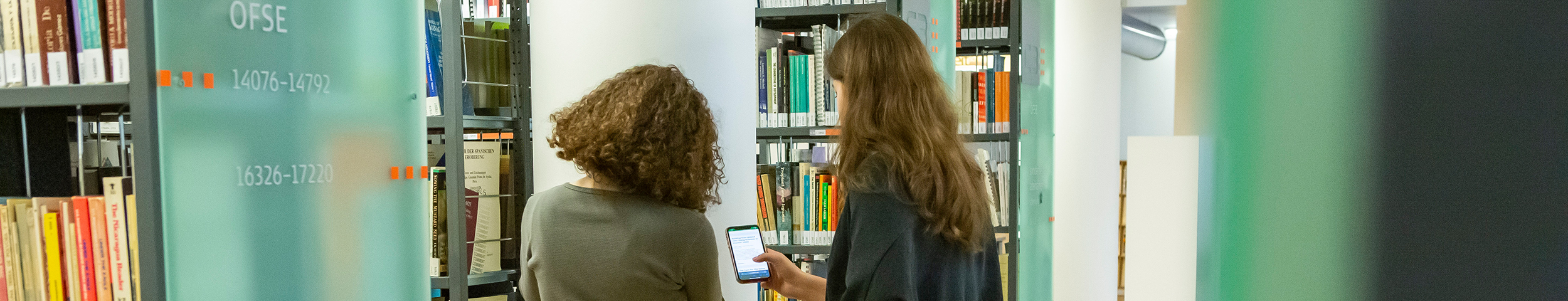 Beratung von einer Nutzer*in der C3 Bibliothek. Die zwei Personen stehen zwischen den Bücherregalen