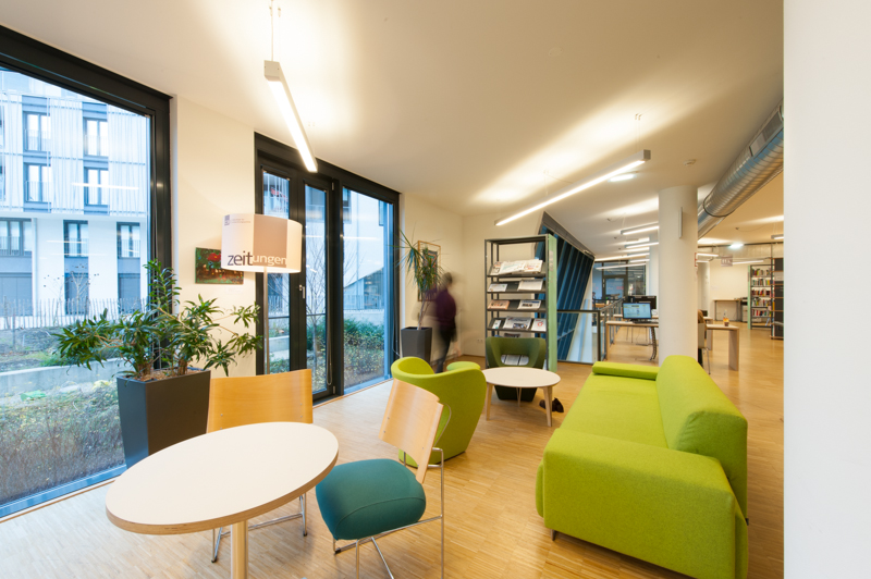 Aufenthaltsecke in der C3 Bibliothek. Zu sehen sind Rundtische und ein großes Sofa
