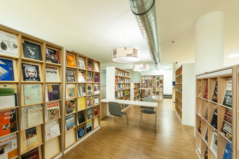 Zu sehen ist der Zeitschriftenbestand der C3 Bibliothek. Die Zeitschriften stehen in Bücherregalen. Zwischen den Regalen steht ein Tisch mit zwei Stühlen.