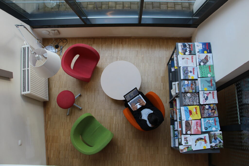 Person die in der C3 in einer Sitzecke am Laptop arbeitet. Neben ihr steht ein Regal, auf dem Südwind Zeitschriften aufgelegt sind