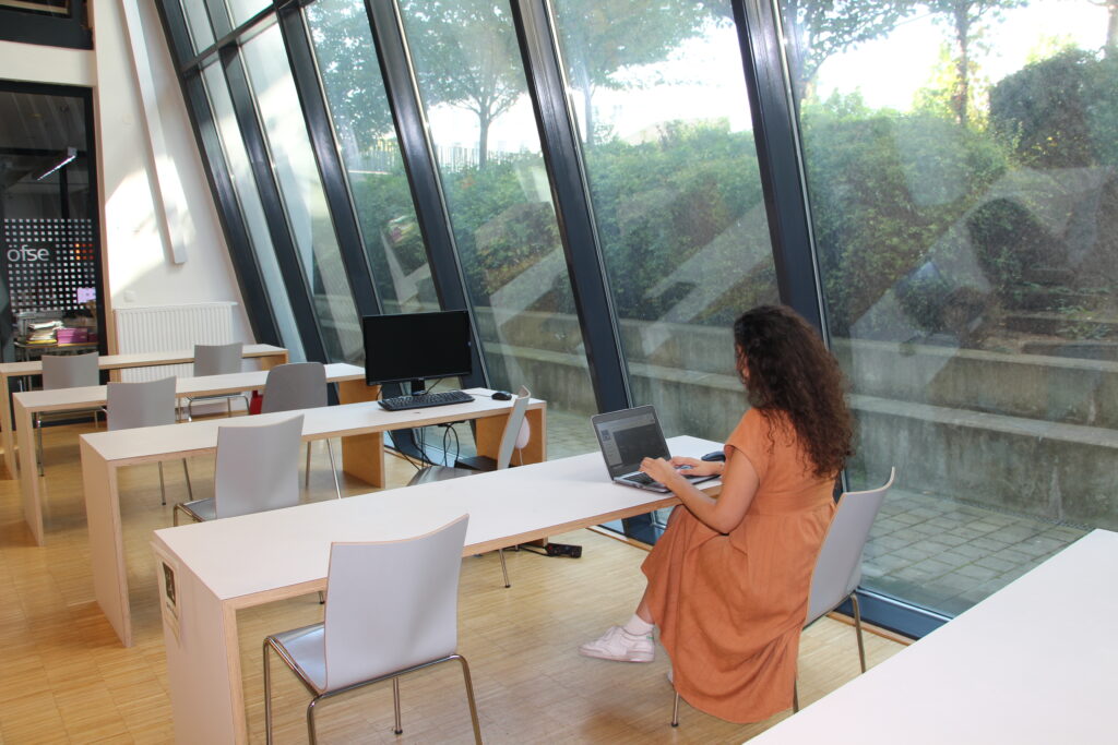 Person, die in der Bibliothek am Tisch sitzt und am Laptop arbeitet