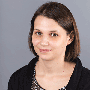 Portrait einer weiblich gelesenen Person vor grauem Hintergrund.